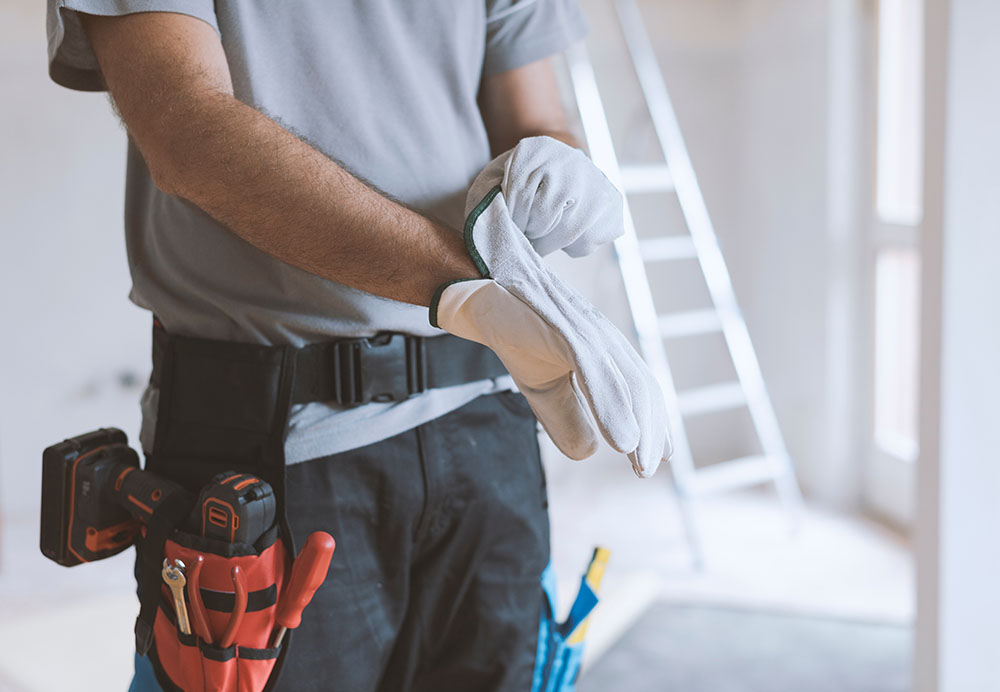 Worker with toolbelt putting on work gloves.