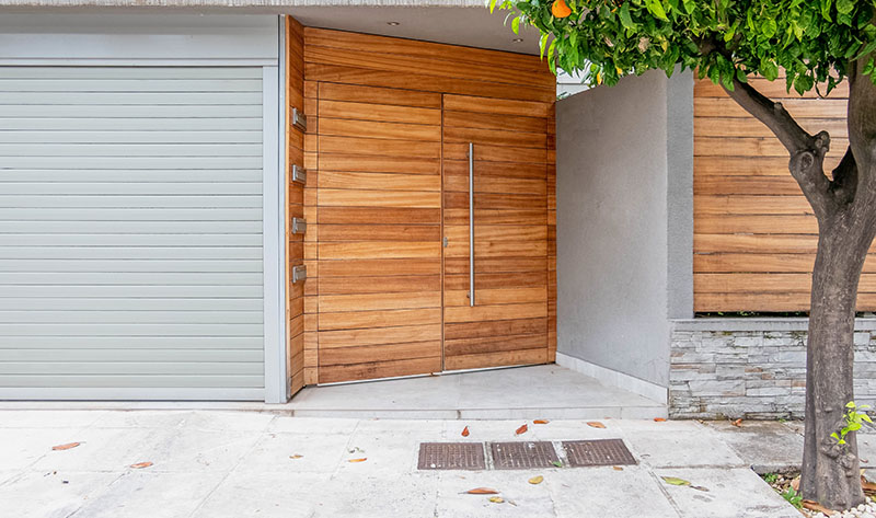 Wood siding around house's front door next to metal garage door.